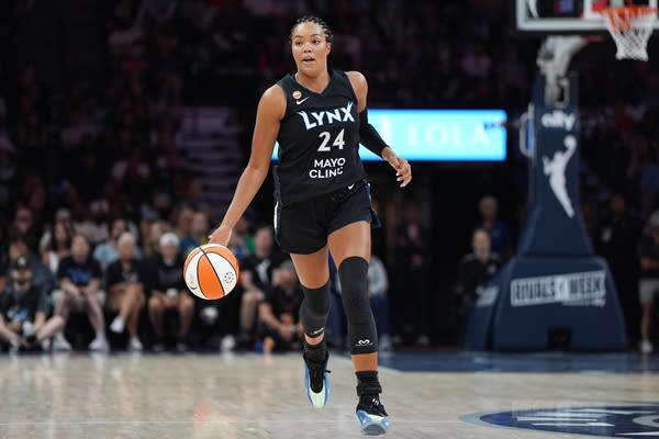 A Lynx basketball player runs down the court toward the camera while dribbling the ball.