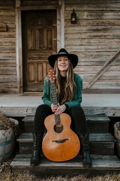 A woman with guitar sitting on the porch of a rustic home