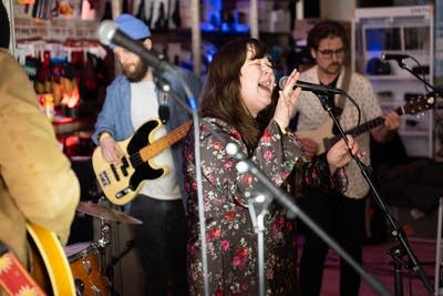 Woman singing microphone, band behind