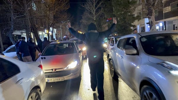 A protester flashes victory signs as traffic slows during demonstrations in Hamedan, Iran on January 1, 2026. 