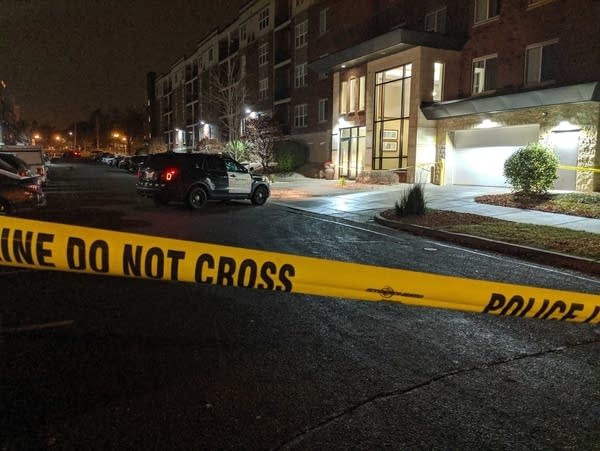 Police tape blocks the view, with a police car in front of an apartment.