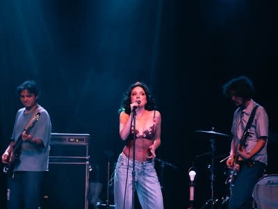 A woman sings into a microphone on a lighted stage.