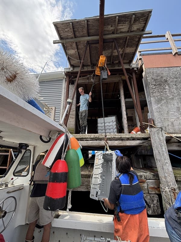 People hoist a gray crate off a boat using a pulley system.