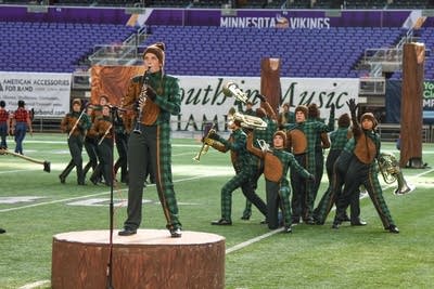 A marching band performs on the field of a football stadium.