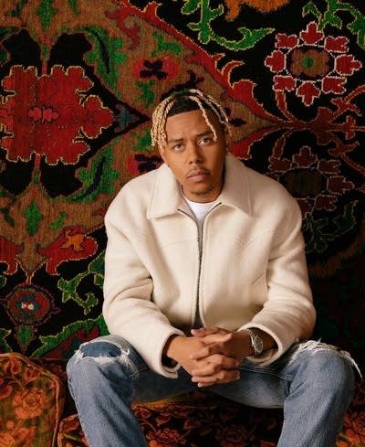 A man sitting on a plush chair in front of a floral tapestry