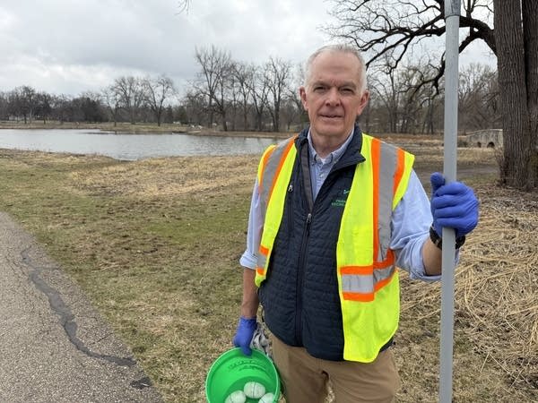 A man in a hi-vis vest holding a green bucket and rake poses for a photo.