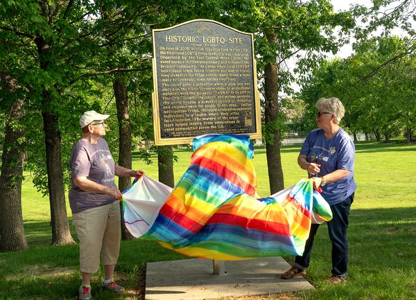 Two people holding Pride flag by an historical marker