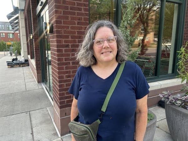 A woman in a blue top smiles for a photo on a street corner.