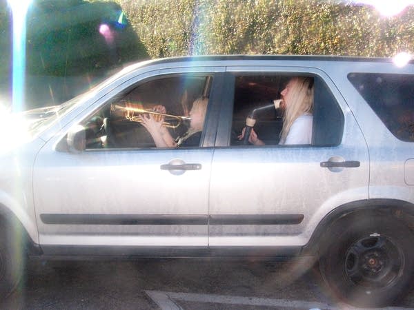 A woman and man sitting in a car playing brass instruments