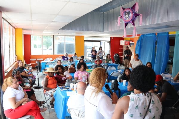 Wide shot of a few dozen people packed into a room with colorful walls and curtains.