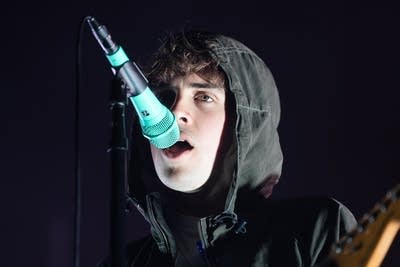 A musician in a hoodie sings into a microphone