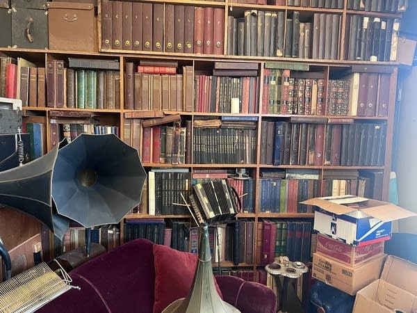 Bookshelves are packed with albums of historical recordings. A phonograph is seen in the foreground.