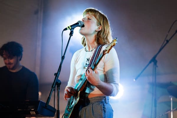 A musician sings and plays guitar on a stage inside a tent
