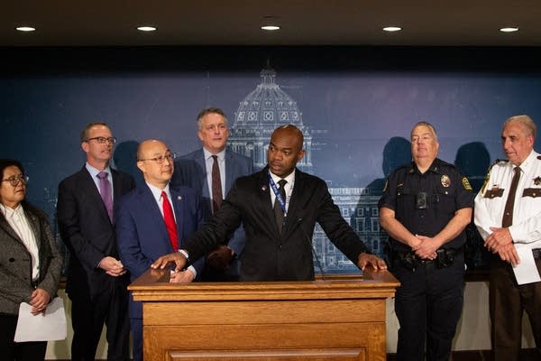 A person speaking at a podium with multiple people behind him