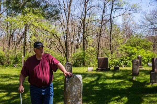 A man rests a hand on a headstone.