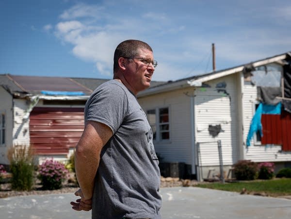 A person stands in front of a damaged house