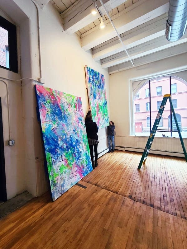 Two people hold up a painting