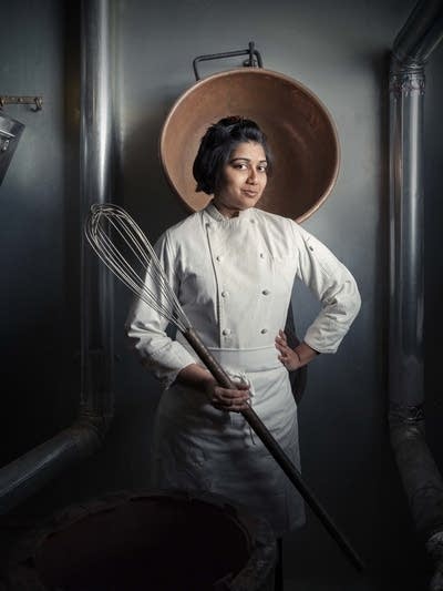 A woman poses for a photo holding a giant whisk. 