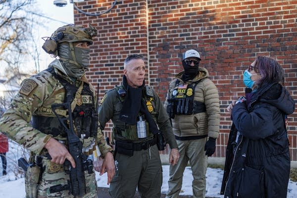 A woman in a mask talks to three Border Patrol agents dressed in military gear.