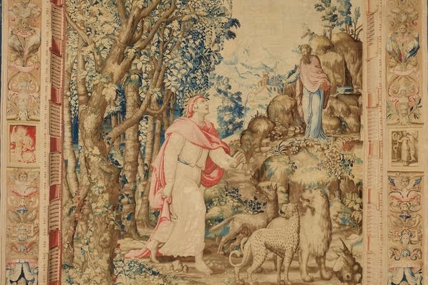 A tapestry artwork. It depicts a man in a red shawl looking up at another man while animals stand nearby.
