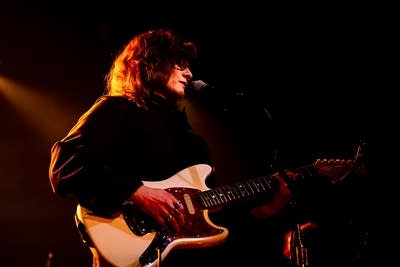 A musician sings and plays guitar onstage in a music venue
