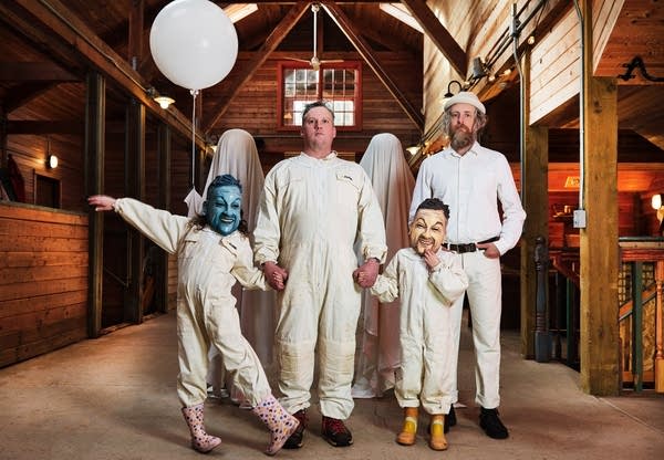 Four people — two of them children in masks — stand in a barn in painters' clothing