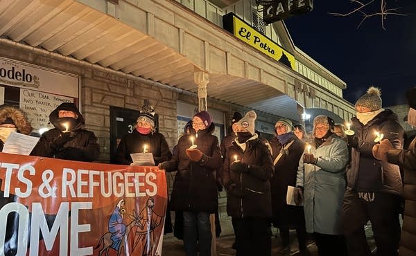 A group of people holds candles at night outside of a closed restaurant.