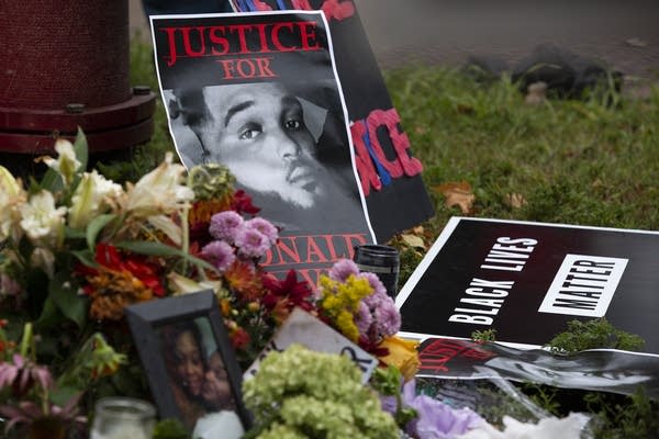 Posters, a framed photograph, and flowers are left on the ground