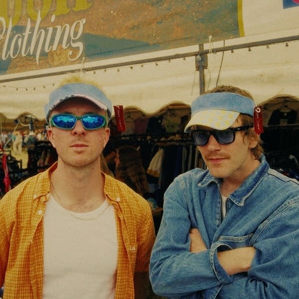 Two guys in visors and sunglasses stand in a street market