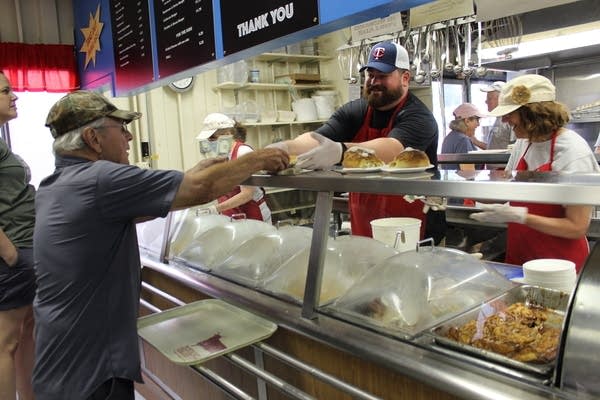 A man stands behind glass and hands another person a tray of food