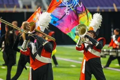 A marching band performs on the field of a football stadium.
