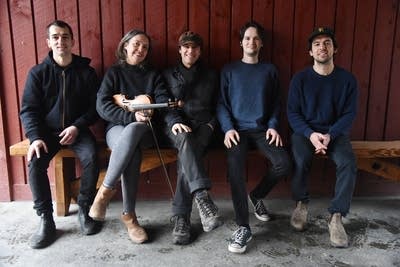 Five people, one with violin, sit together on a bench for a group photo