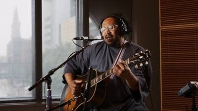 A musician sings and plays guitar in a recording studio