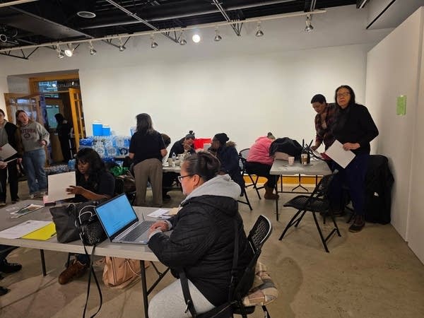 People fill out forms on laptops while sitting around tables.