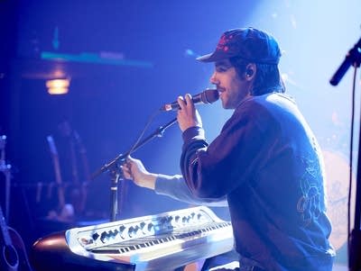 A man plays an keyboard and sings into a microphone.