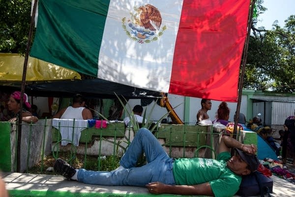 Migrants taking part in a caravan heading to the US, rest next to a Mexican national flag. (Photo by Guillermo Arias / AFP)