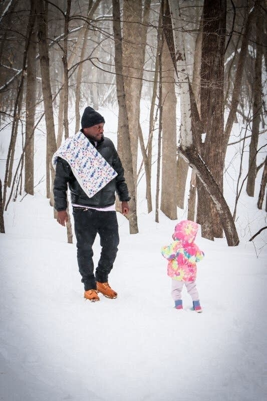 A man walks in a snowy woods with a young child in pink.