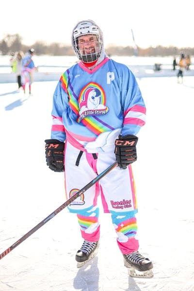 A hockey player in a blue, pink and white uniform poses for a photo.