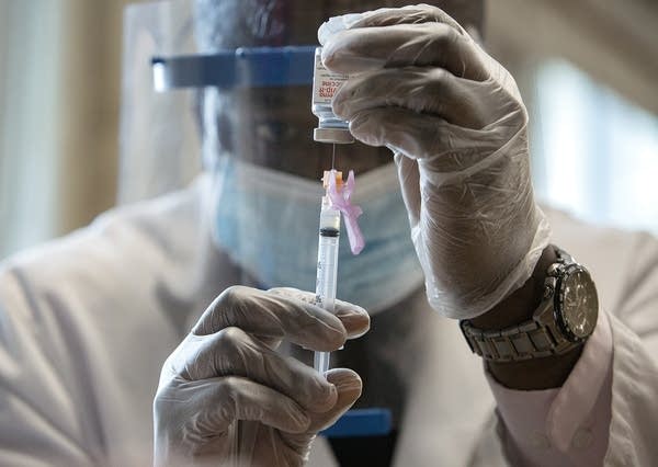 A man puts a needle in a glass vial. 