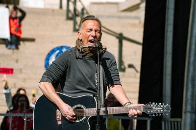 A man sings and plays guitar on an outdoor stage at a large rally