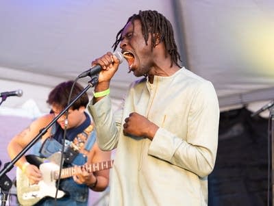 Papa Mbye sings into a microphone with his eyes closed.
