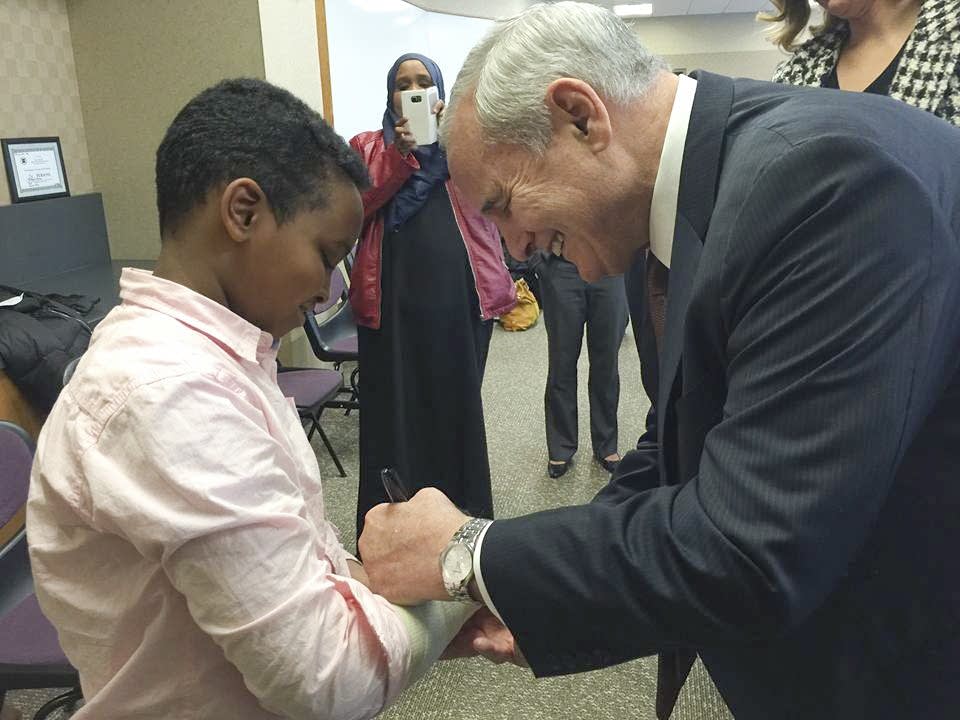 Gov. Mark Dayton signs Yusuf Dayur's cast in 2015.