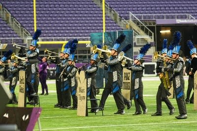 A marching band performs on the field of a football stadium.