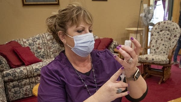 A woman in a mask fills a syringe with vaccine from a vial