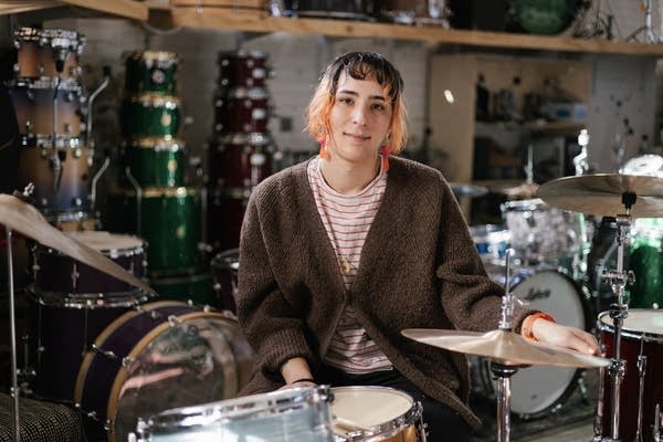 a woman posing by a drum set surrounded by drum equipment