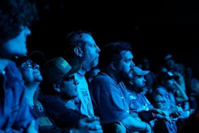A row of music fans stand bathed in light while enjoying a concert