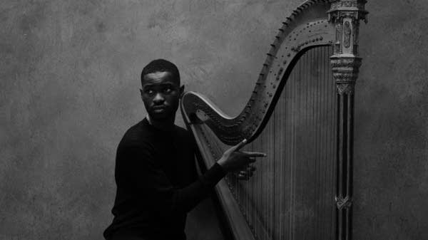 Poster British rapper Dave poses next to a classical harp