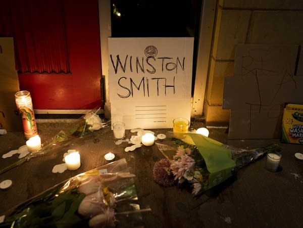 A cardboard sign with "Winston Smith" written on it, surrounded by candles.