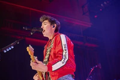 A musician sings and plays guitar onstage in a large music venue