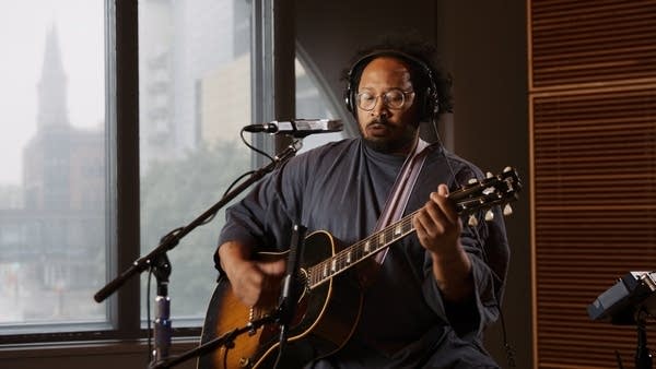 A musician sings and plays guitar in a recording studio